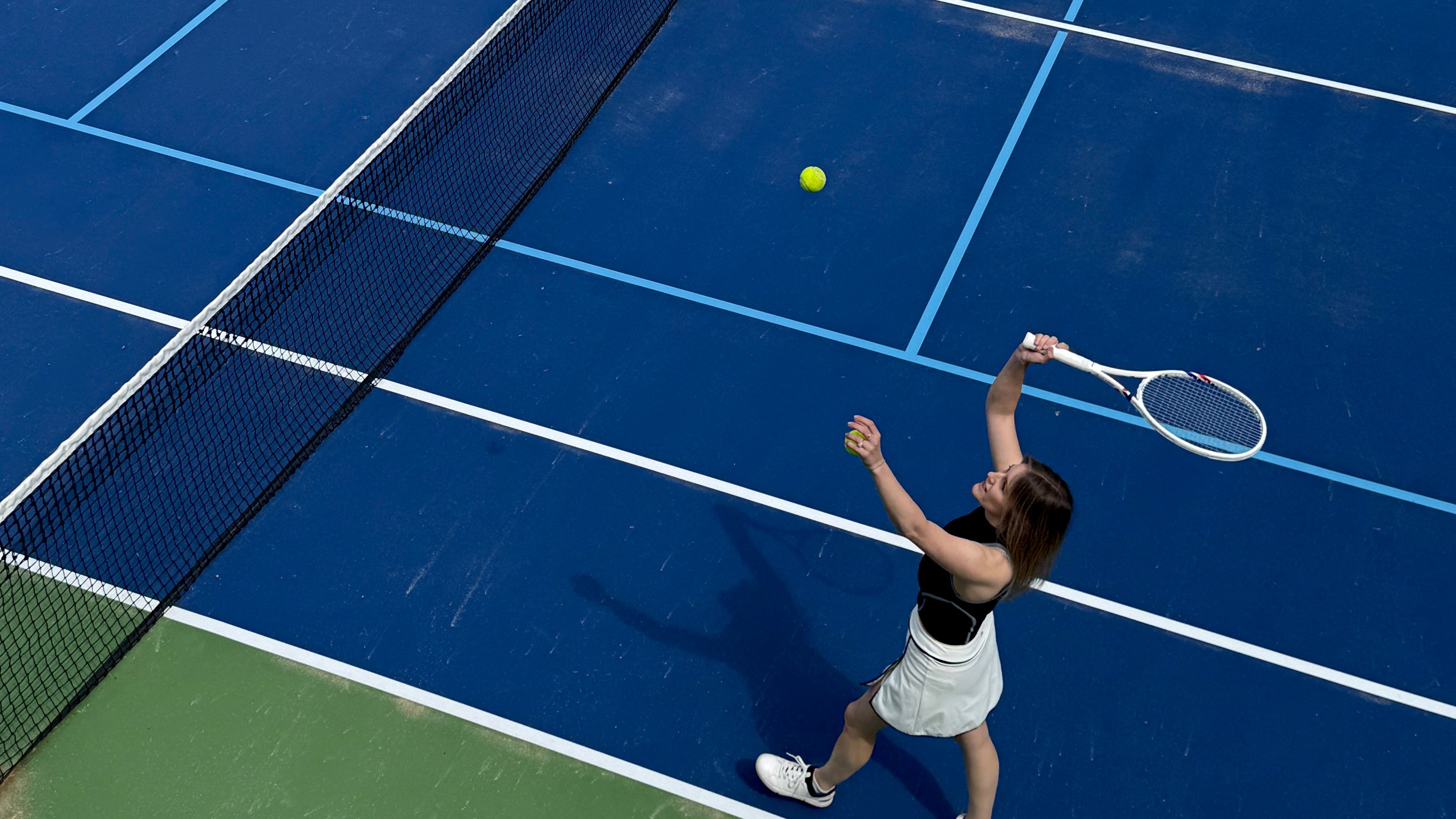 Person playing tennis on a blue court with a green surface